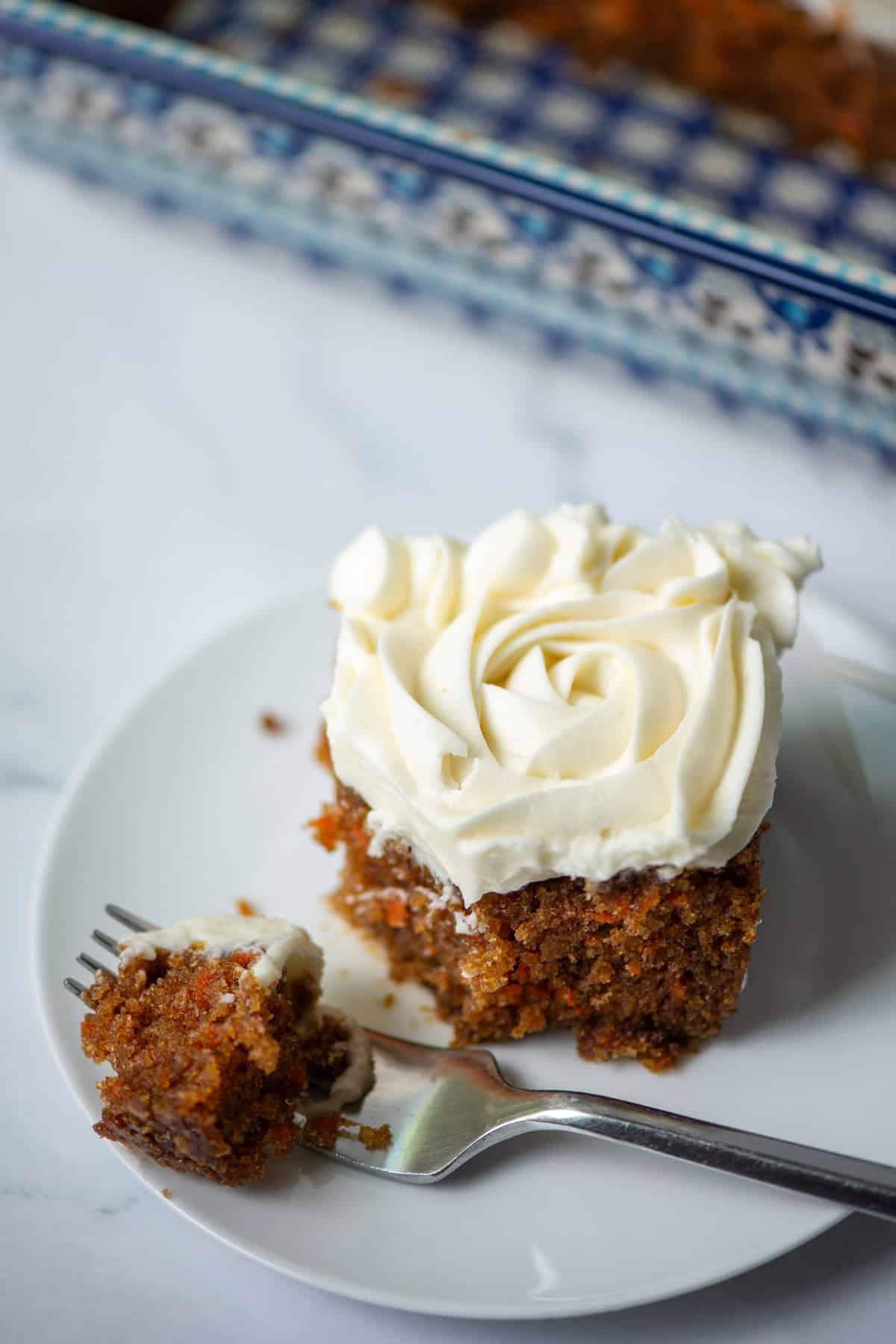 Overhead photo of slice of carrot cake on a plate in front of a baking pan of carrot cake