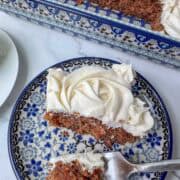 Overhead photo of slice of carrot cake on a plate in front of a baking pan of carrot cake with three pieces missing