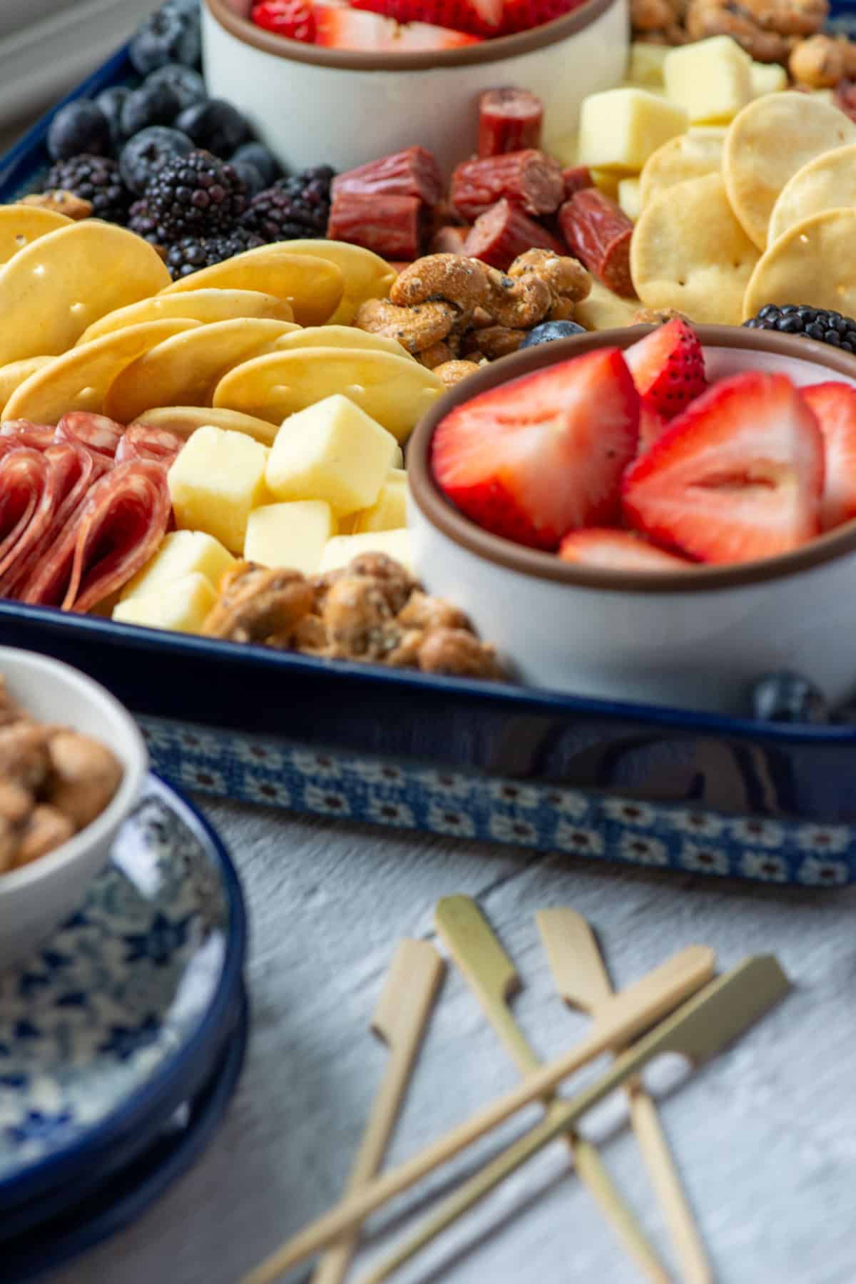 Side view of a portion of a charcuterie board made with ingredients from Aldi next to some plates and some small decorative skewers
