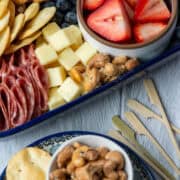 Overhead photo of a plate with nuts and pita chips next to a charcuterie board made with ingredients from Aldi and some small decorative skewers