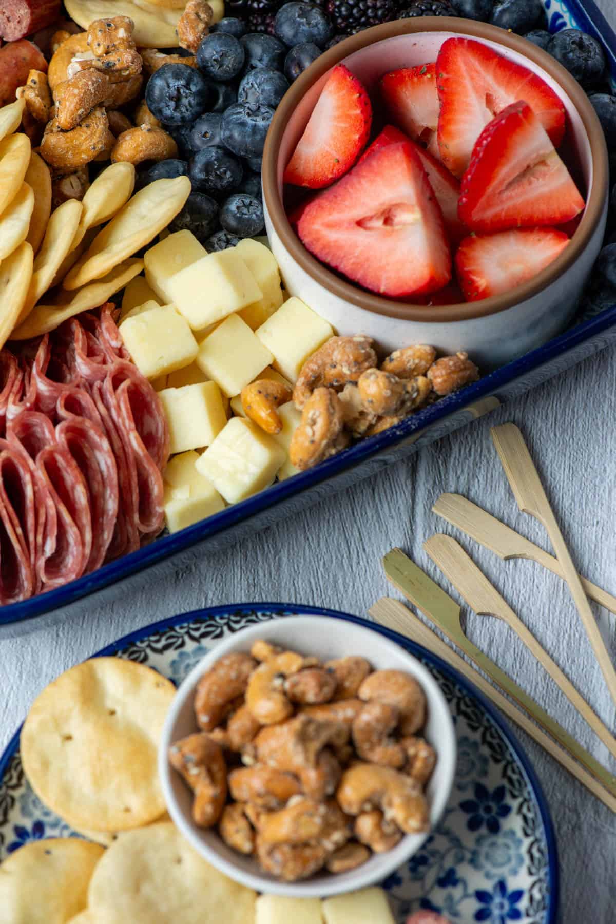 Overhead photo of a plate with nuts and pita chips next to a charcuterie board made with ingredients from Aldi and some small decorative skewers