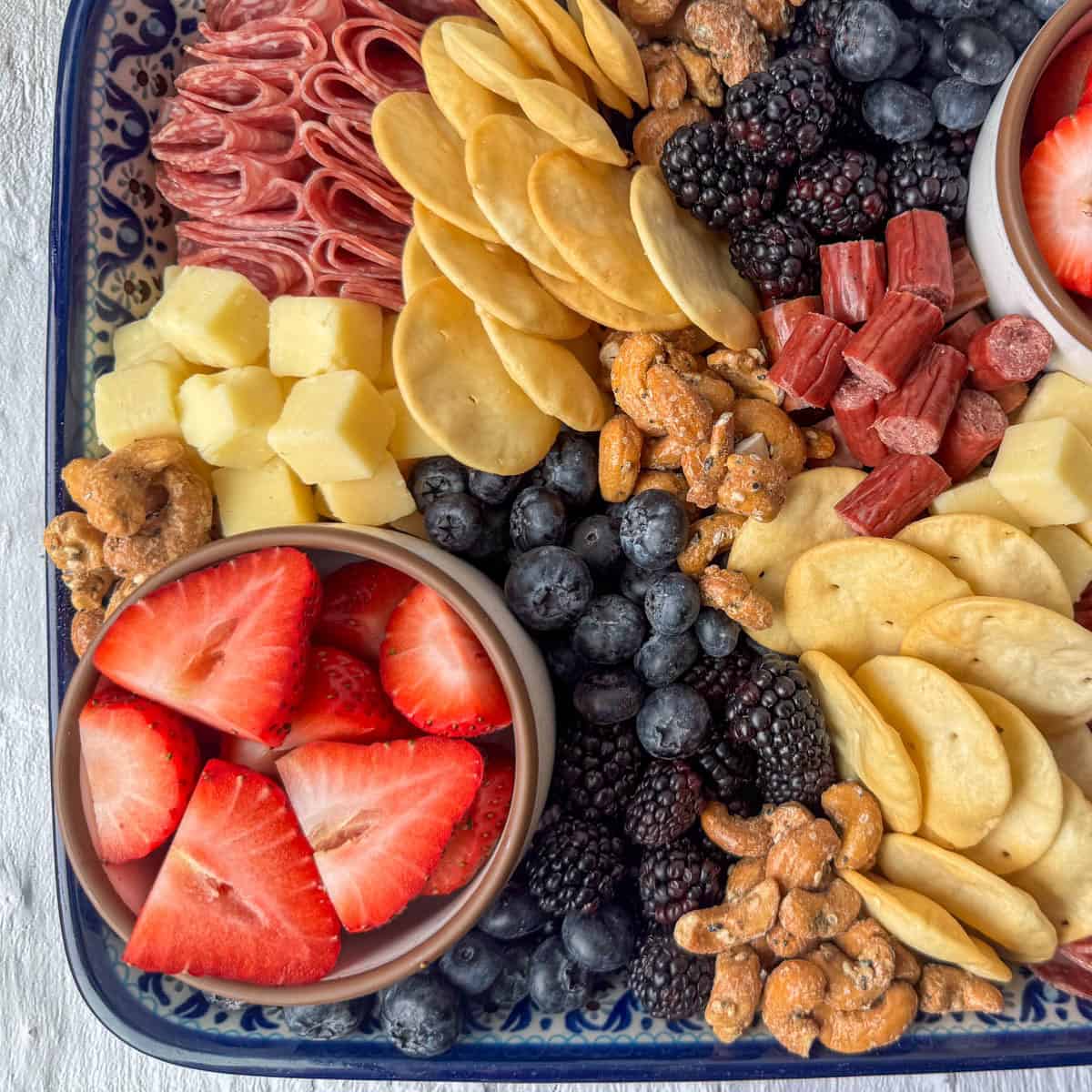 Overhead photo of a part of Charcuterie Board made from ingredients from Aldi: strawberries, blackberries, blueberries, cheese cubes, pita chips, nuts, meat sticks and cured meats