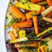 Close up overhead view of chopped hot honey roasted carrots on a serving platter with parsley garnish