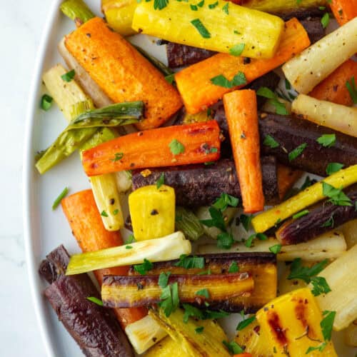 Close up overhead view of chopped hot honey roasted carrots on a serving platter with parsley garnish