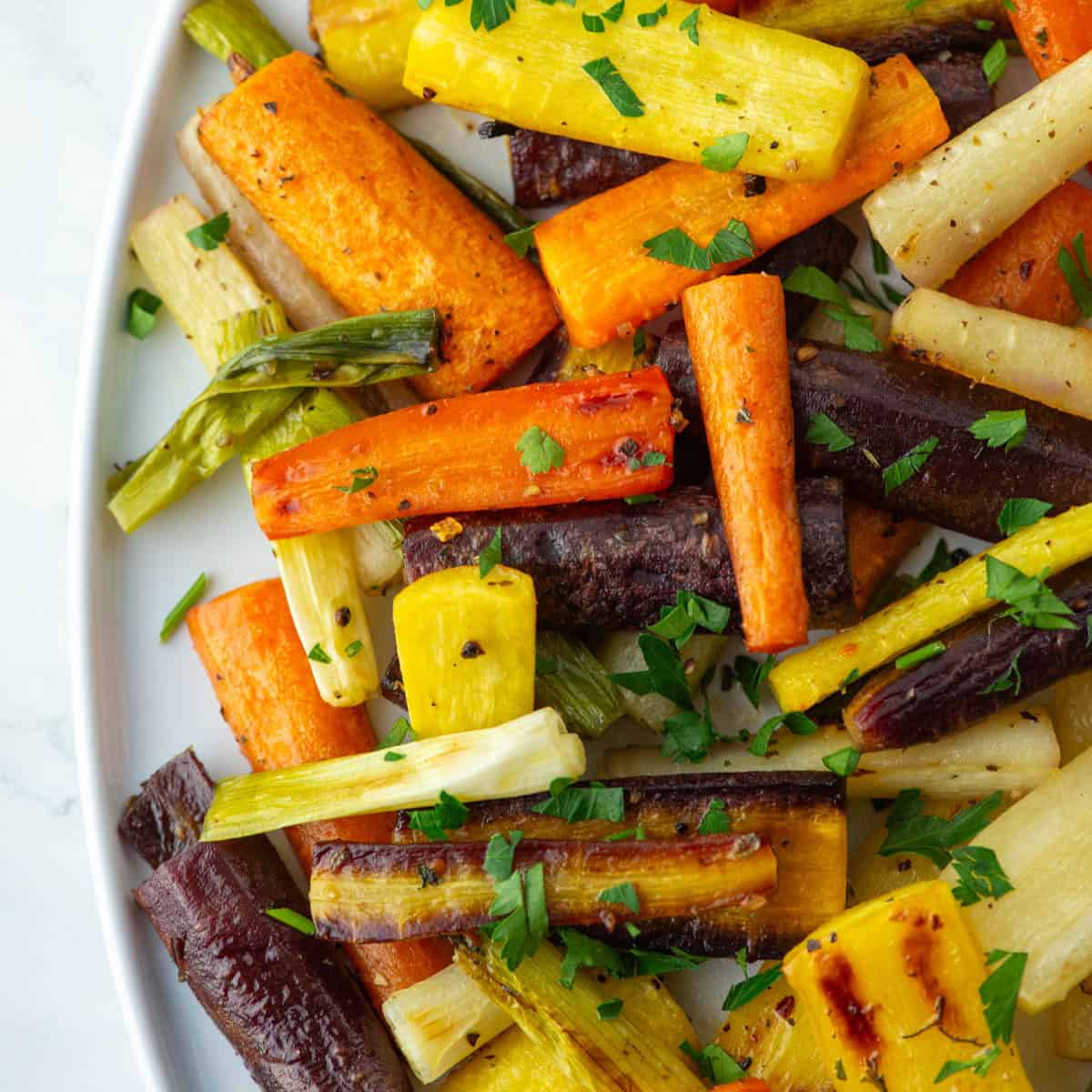 Close up overhead view of chopped hot honey roasted carrots on a serving platter with parsley garnish