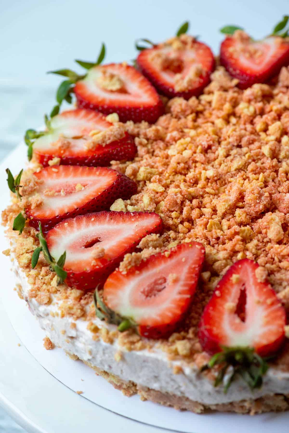 Overhead view of half of a no-bake strawberry cheesecake topped with strawberry crunch and cut strawberries