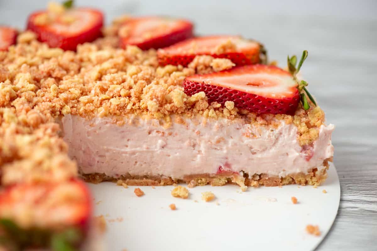 Side view of a cut no-bake strawberry crunch cheesecake topped with strawberry crunch and cut strawberries on a serving platter