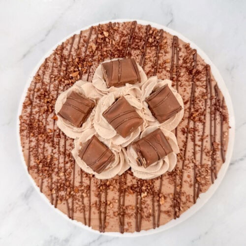 Overhead photo of No Bake Nutella Cheesecake topped with Nutella drizzle, hazelnut crumbs, Nutella whipped cream and Kinder Buenos