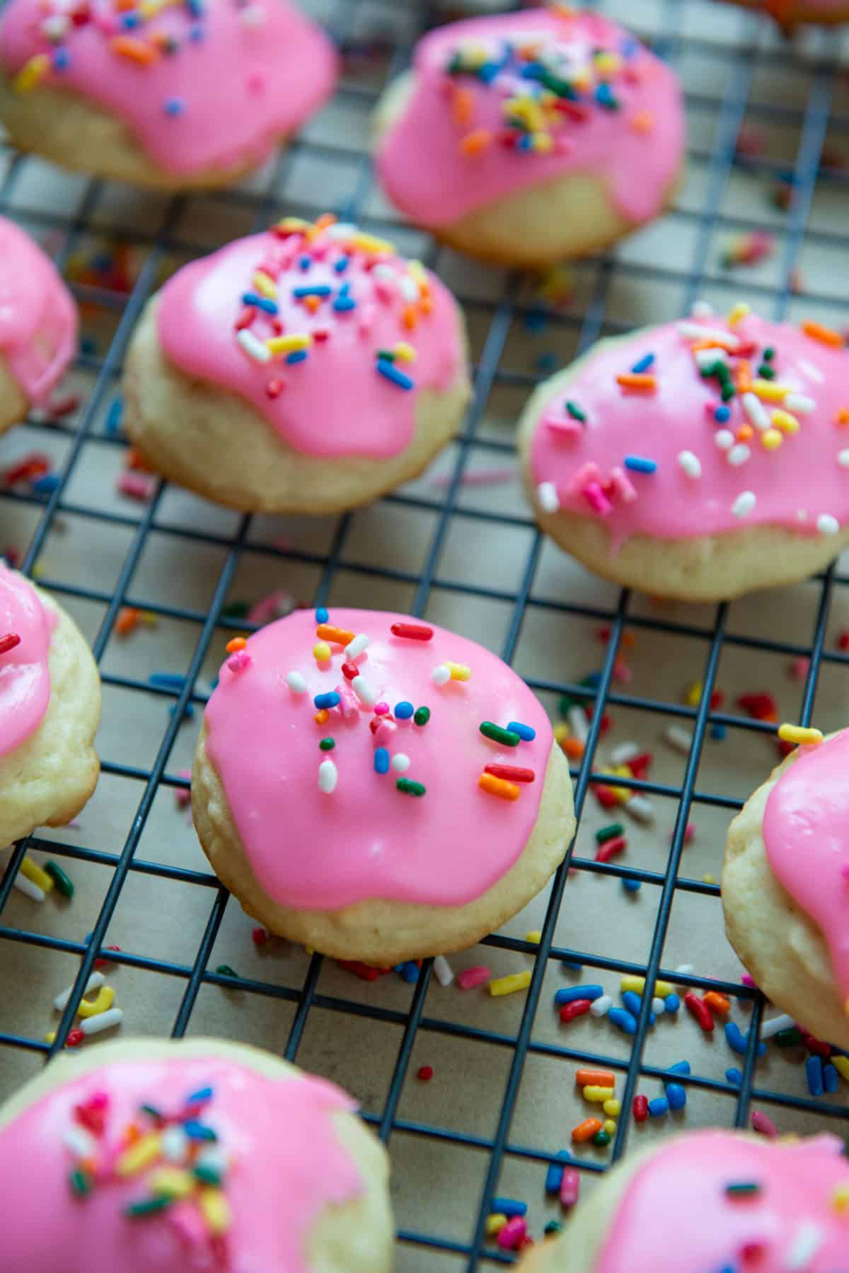 Sour cream cookies with pink frosting and multicolored sprinkles on a cooling rack