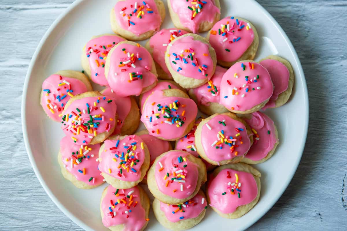 Overhead photo of sour cream cookies with pink frosting and multicolored sprinkles on a serving plate