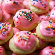 Sour cream cookies with pink frosting and multicolored sprinkles stacked up on a serving plate