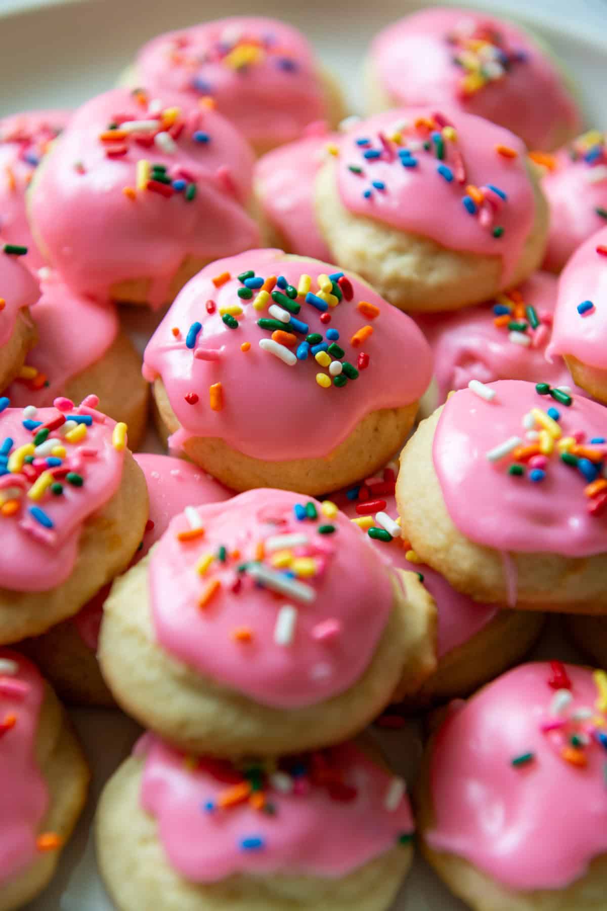 Sour cream cookies with pink frosting and multicolored sprinkles stacked up on a serving plate