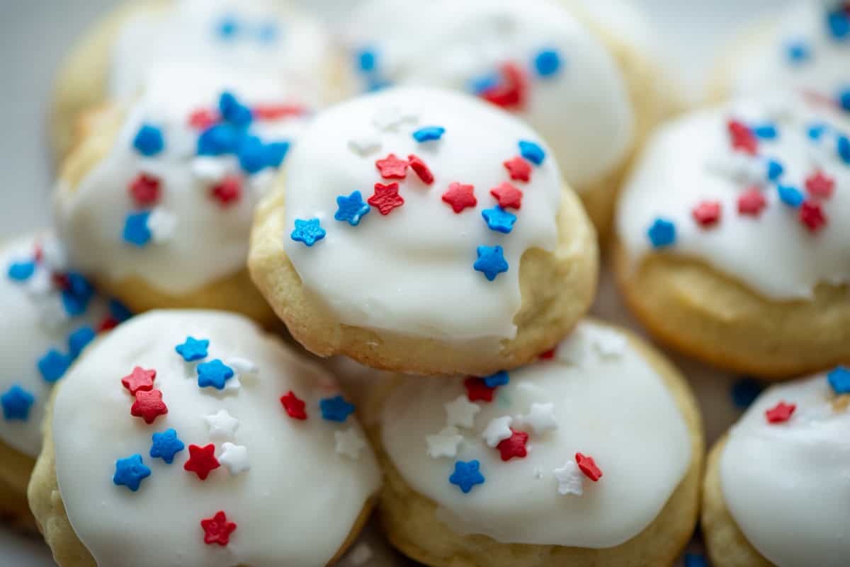 Close up photo of sour cream cookies with white frosting and red, white and blue star sprinkles stacked up