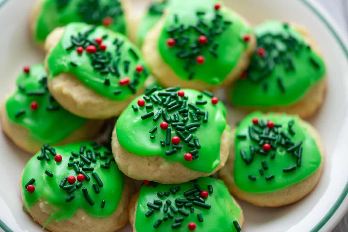 Close up photo of sour cream cookies with leaf green frosting and red and green sprinkles stacked up on a plate