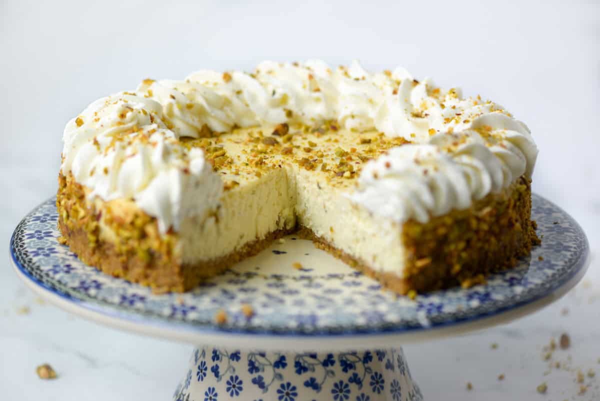 Side view of a cut pistachio cheesecake on a dessert stand