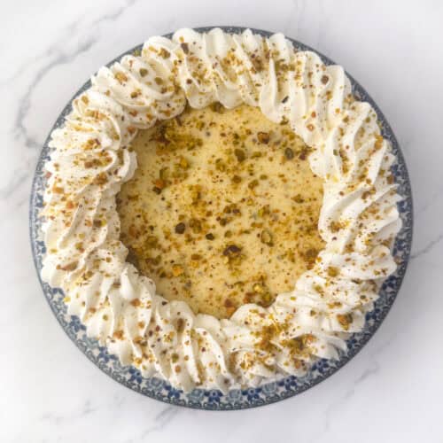 Overhead view of a pistachio cheesecake topped with whipped heavy cream and pistachio crumbs