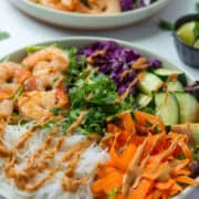 Angled view of entree size plate of Spring Roll Salad drizzled with peanut dressing, next to a small bowl of limes and another plate of Spring Roll Salad