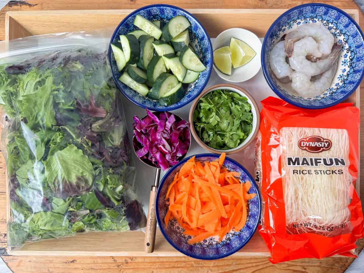Ingredients needed for Spring Roll Salad: shrimp, rice stick noodles, carrots, cucumbers, cabbage, limes, cilantro and lettuce
