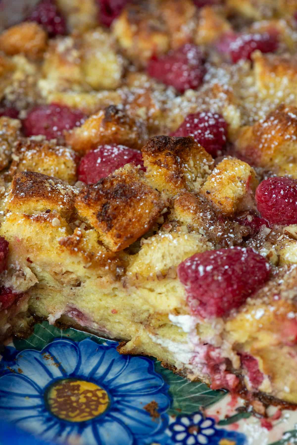 45 degree view of a pan of baked raspberry brioche French toast casserole that has two pieces missing so the you can see the multiple layers of brioche, goat cheese and raspberries. 