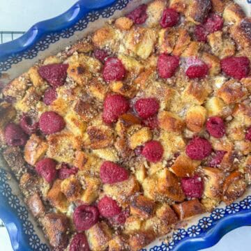 Overhead photo of baked raspberry brioche French toast casserole in a fancy blue rimmed baking pan