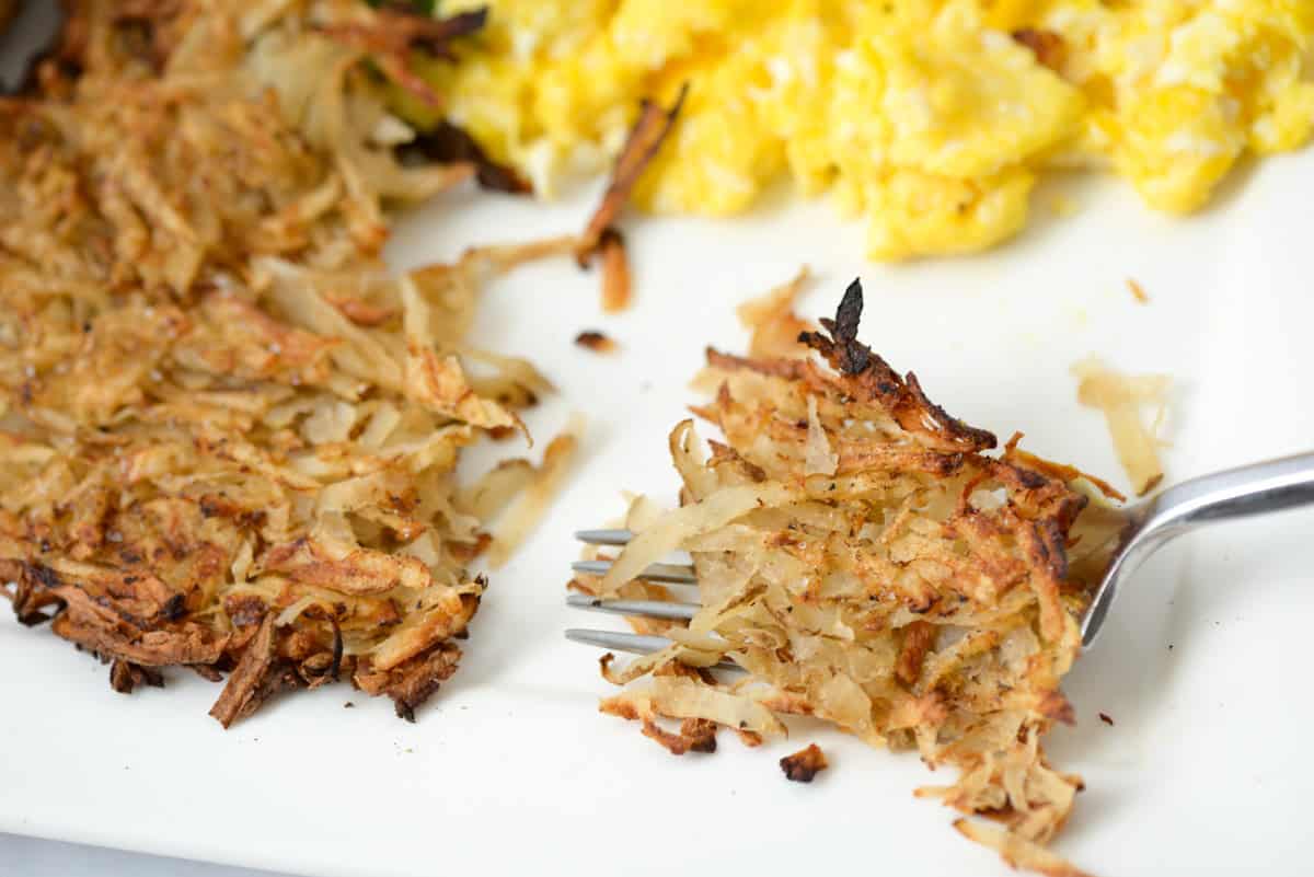 Close up view of grilled hash brown next to scramble eggs with a bite of hash browns on a fork