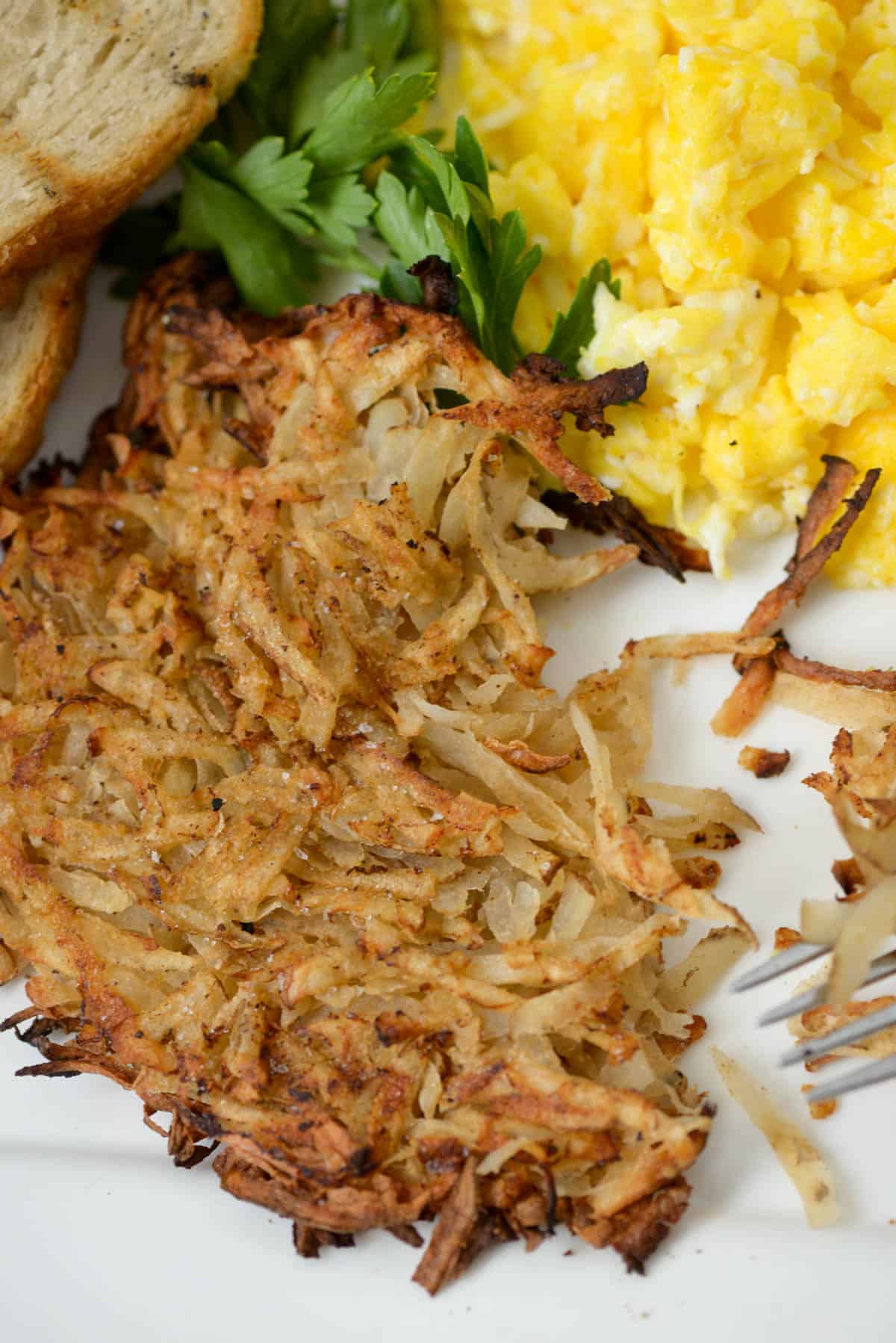 Overhead view of a partially eaten hash brown next to eggs, toast and parsley garnish