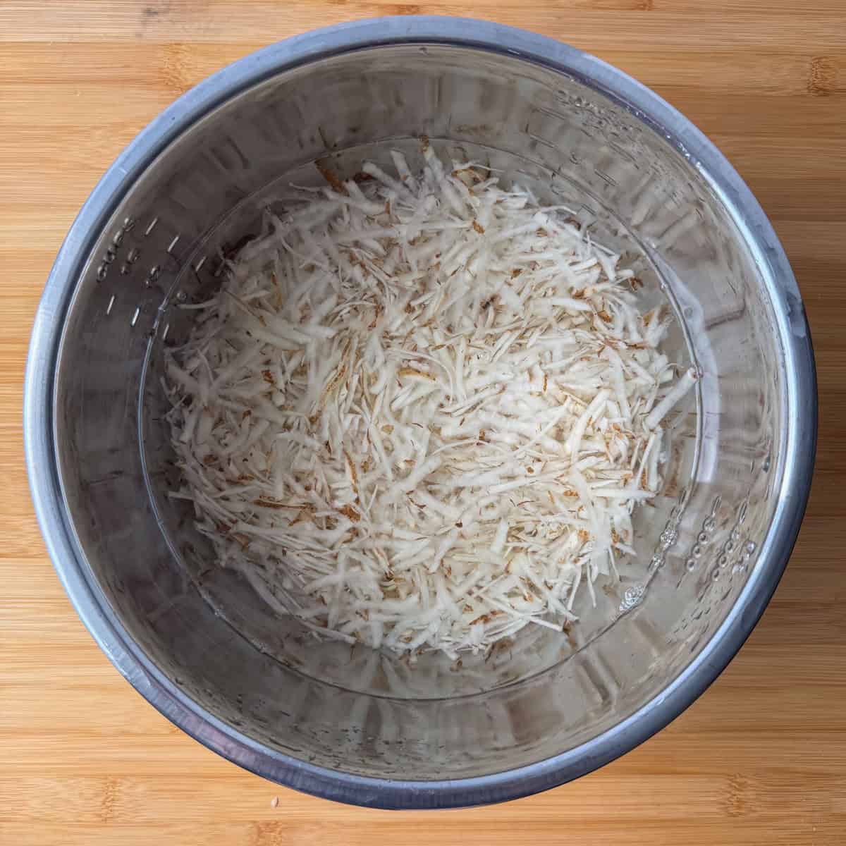 Overhead view of potatoes soaking in water after third rinse