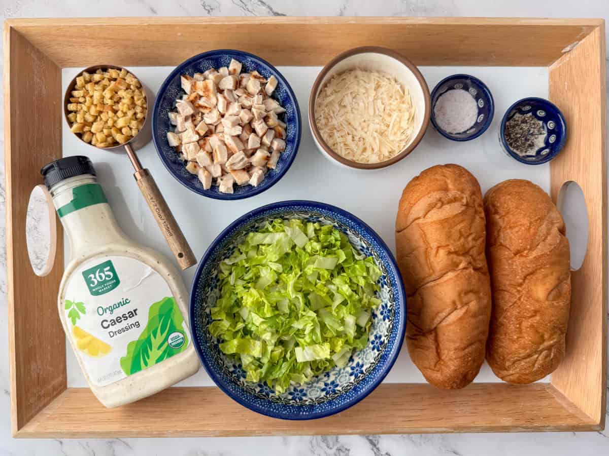 Ingredients needed to make a chicken caesar salad sandwich: cooked and cubed chicken, Parmesan Cheese, mini croutons, romaine lettuce, Caesar dressing, hoagie buns, salt and pepper. 