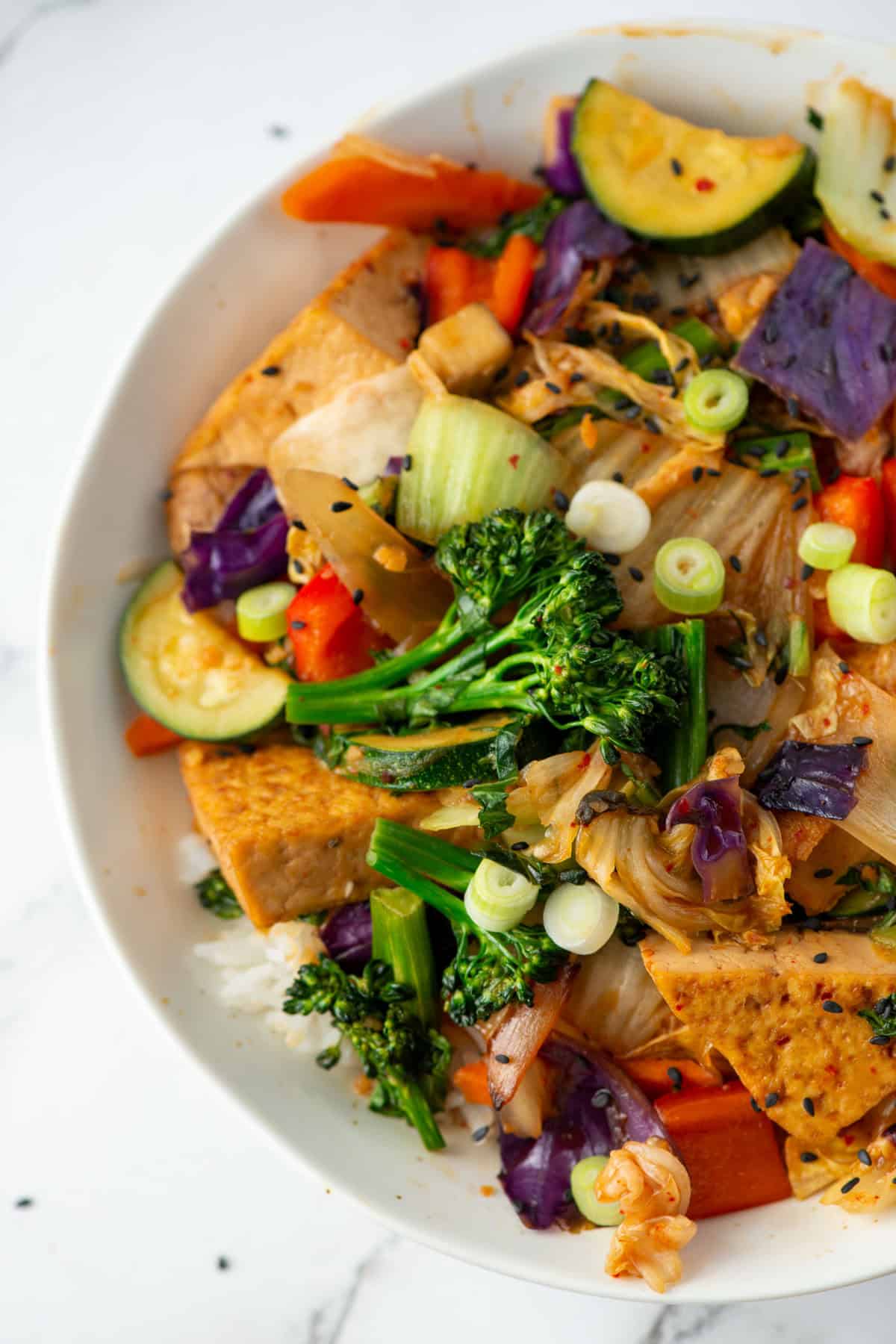 Overhead close up view of half of the bowl of kimchi tofu stir fry with vegetables