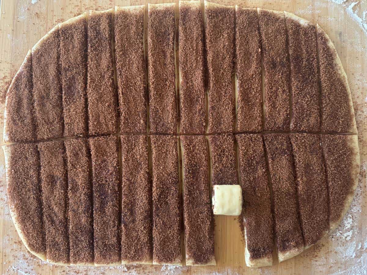 Overhead view of rolled out cinnamon roll dough topped with the butter, brown sugar and cinnamon filling and cut into twelve strips using a pizza cutter