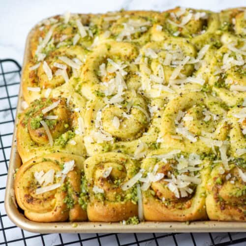 View of a partial baking pan on mini pesto rolls topped with Parmesan Cheese and cracked pepper