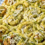Overhead view of a baked pan of mini pesto rolls topped with more pesto, grated Parmesan Cheese and cracked black pepper