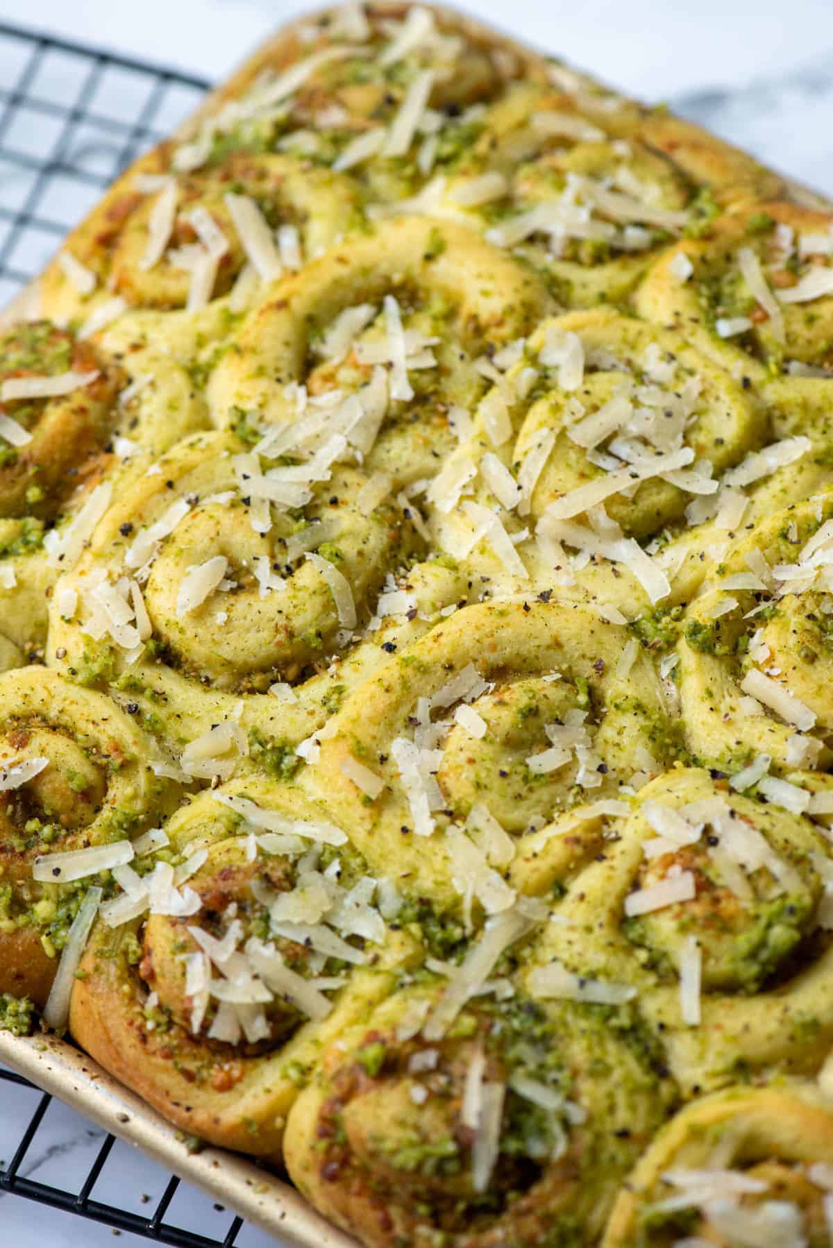 Overhead view of a baked pan of mini pesto rolls topped with more pesto, grated Parmesan Cheese and cracked black pepper