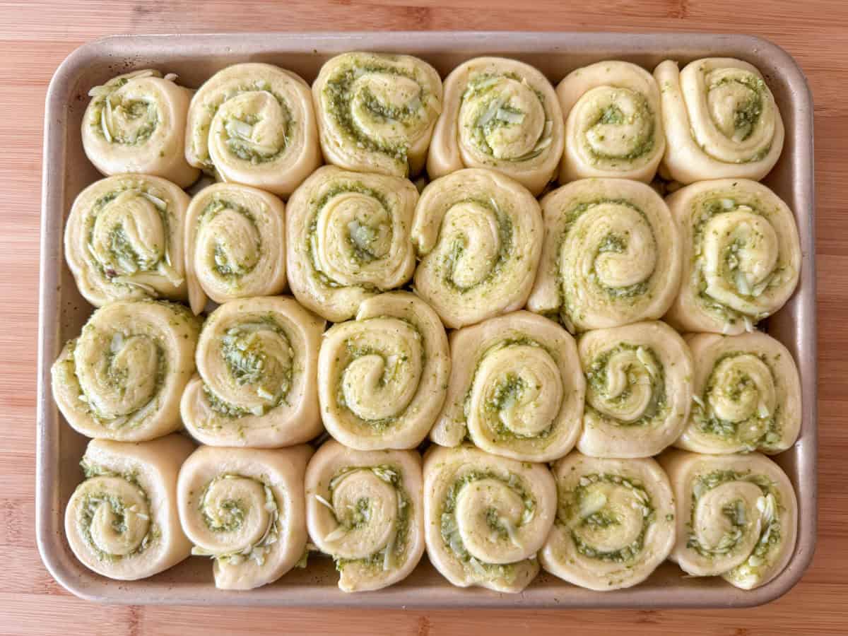 Overhead view of unbaked pesto rolls in a ¼ baking sheet 