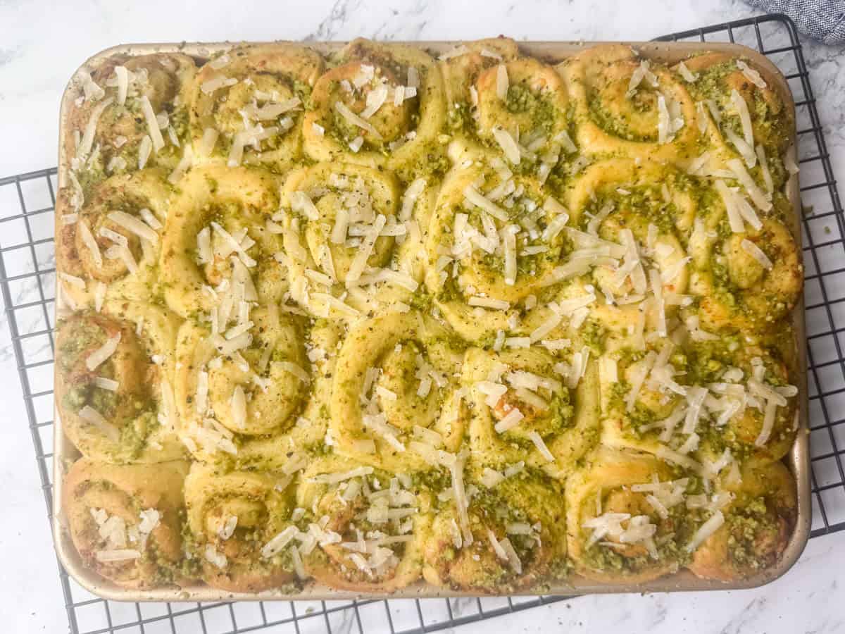 Overhead view of a fill ¼ sheet baking pan of baked mini pesto rolls topped with Parmesan Cheese and cracked pepper