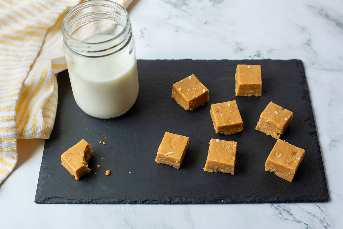 Cut peanut butter fudge squares topped with salt flakes and a glass of milk on a slate plate with a napkin in the background