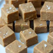 Cut peanut butter fudge squares topped with salt flakes stacked on top of each other on a serving plate