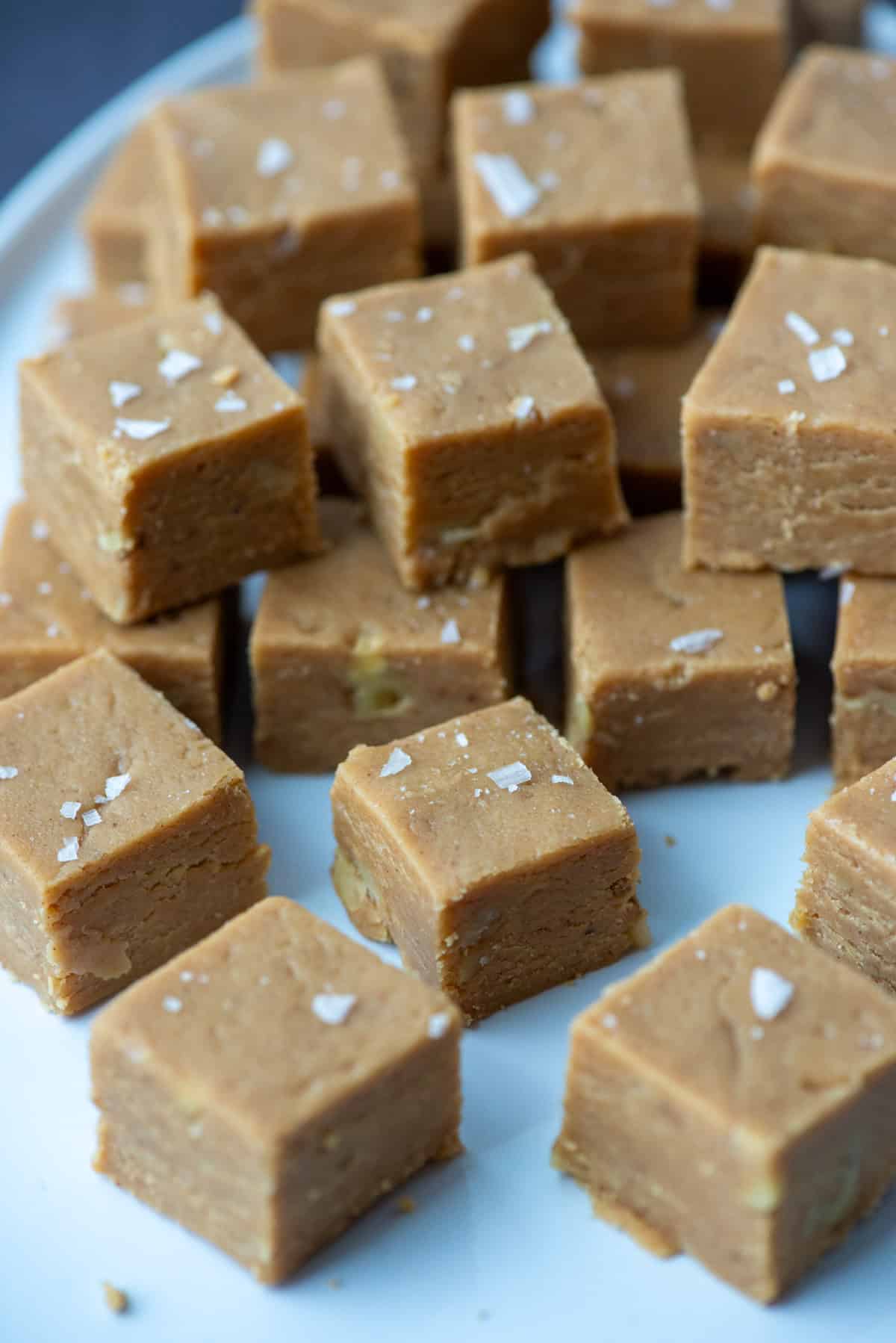 Cut peanut butter fudge squares topped with salt flakes stacked on top of each other on a serving plate
