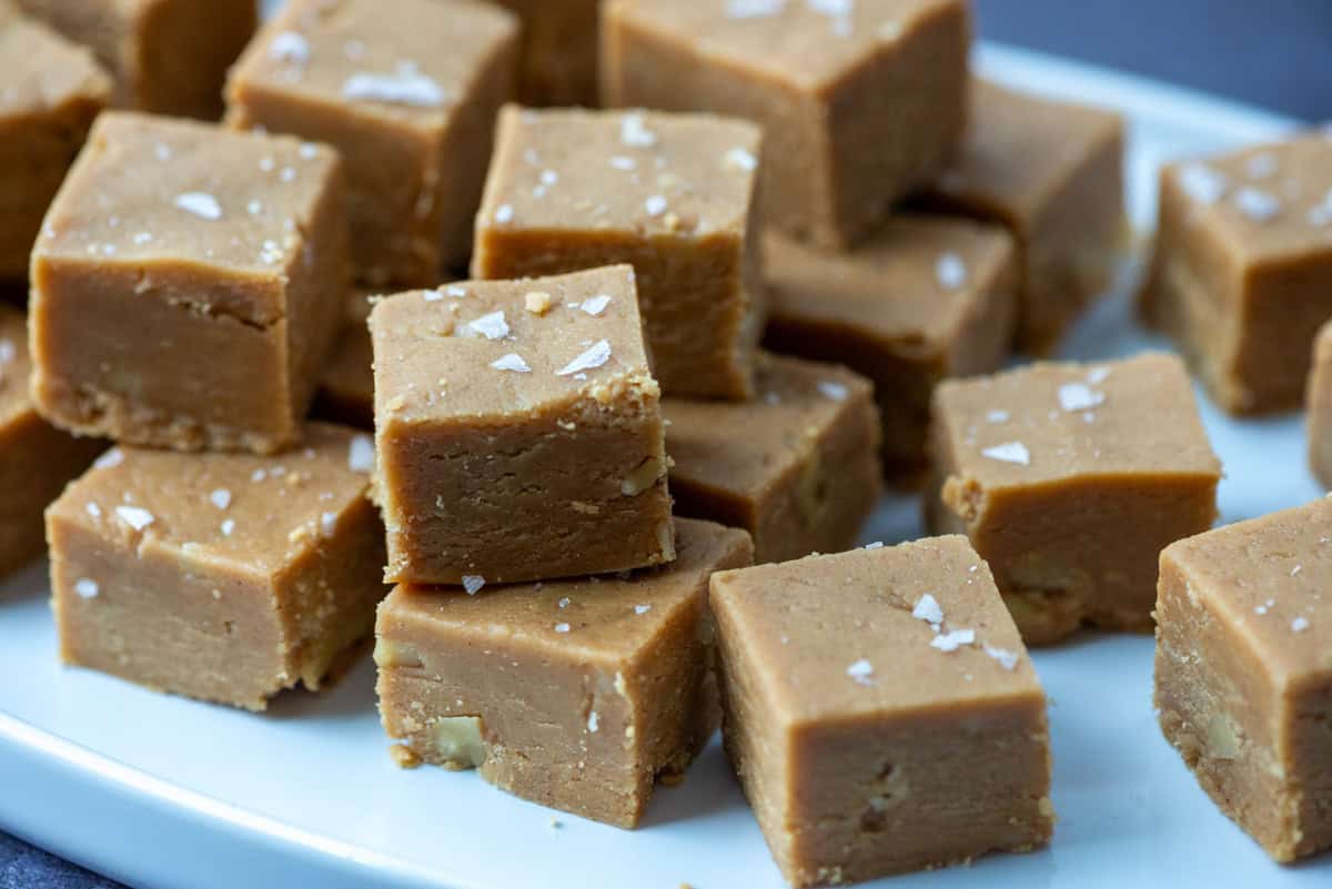 Cut peanut butter fudge squares topped with salt flakes stacked on top of each other on a serving plate