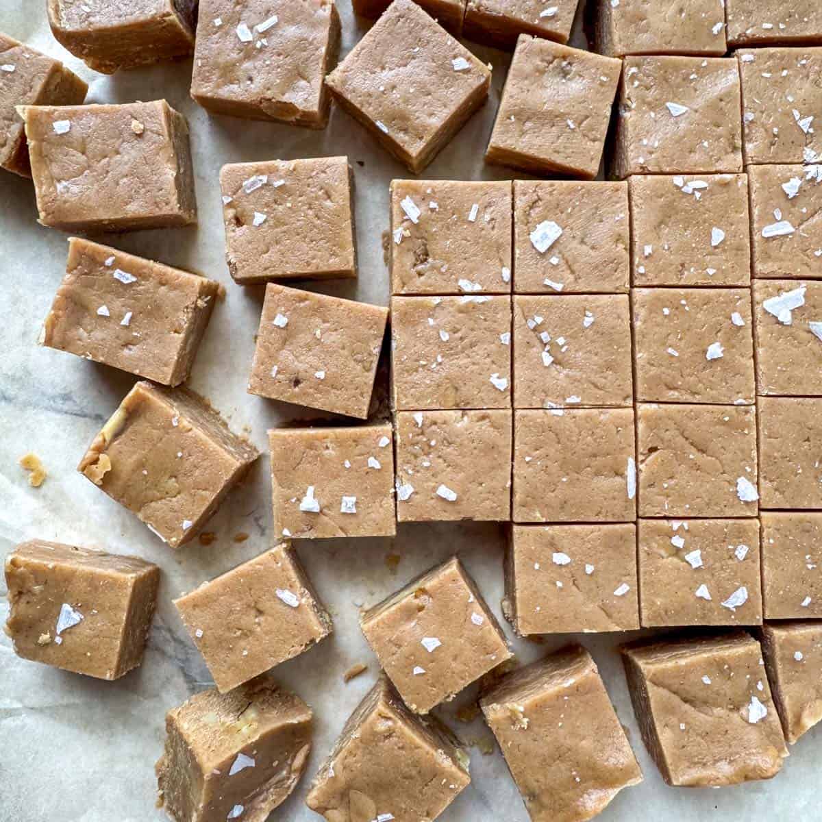 Cut peanut butter fudge squares topped with salt flakes on parchment paper