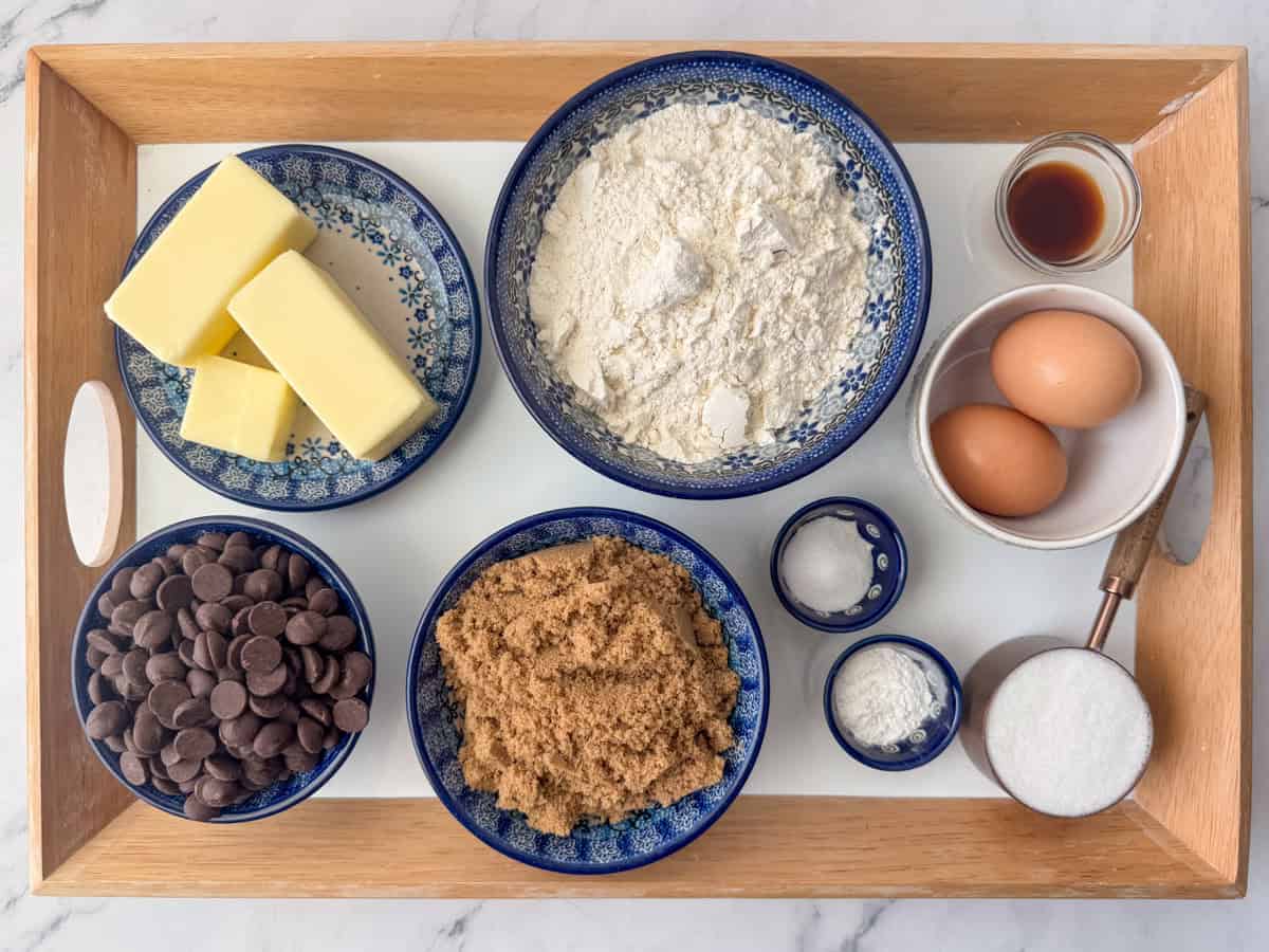Overhead photo of ingredients needed to make brown butter chocolate chip bars: butter, brown sugar, white sugar, eggs, vanilla, all-purpose flour, baking powder, salt and chocolate chips.