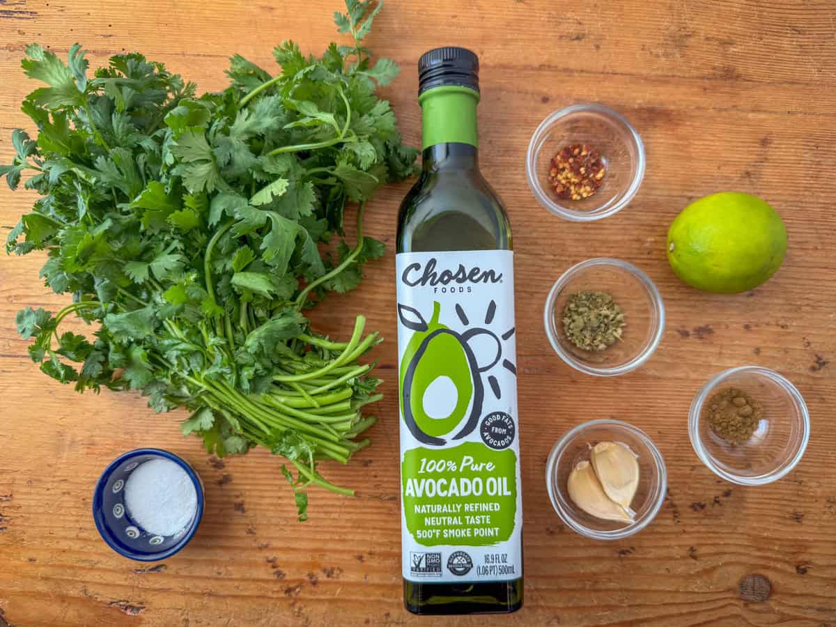 Ingredients needed to make chimichurri sauce: fresh cilantro, avocado oil, lime, garlic, Mexican oregano, cumin, crushed red pepper and salt.