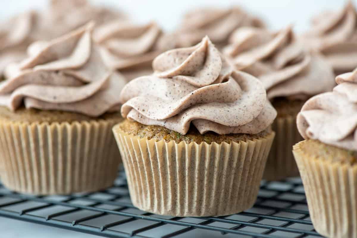 Close up side view of zucchini cupcakes with cinnamon cream cheese frosting closely together on a cooling rack