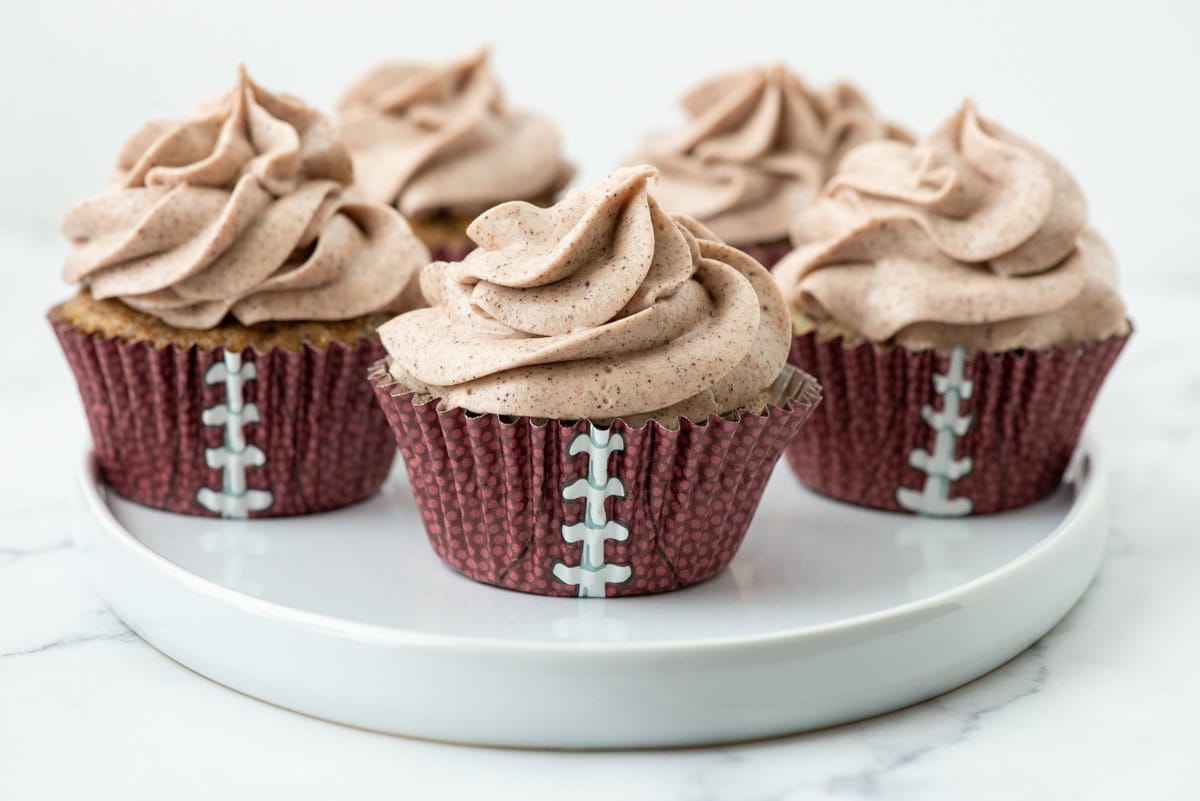Five zucchini cupcakes, using football themed cupcake liners, with cream cheese frosting on a serving plate