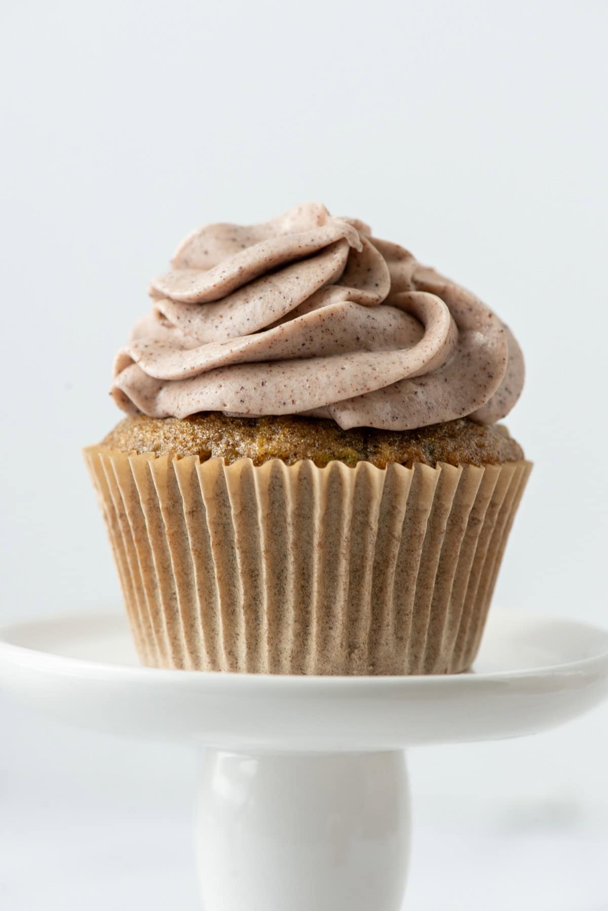 Side view of one single zucchini cupcake with cinnamon cream cheese frosting on a small dessert stand