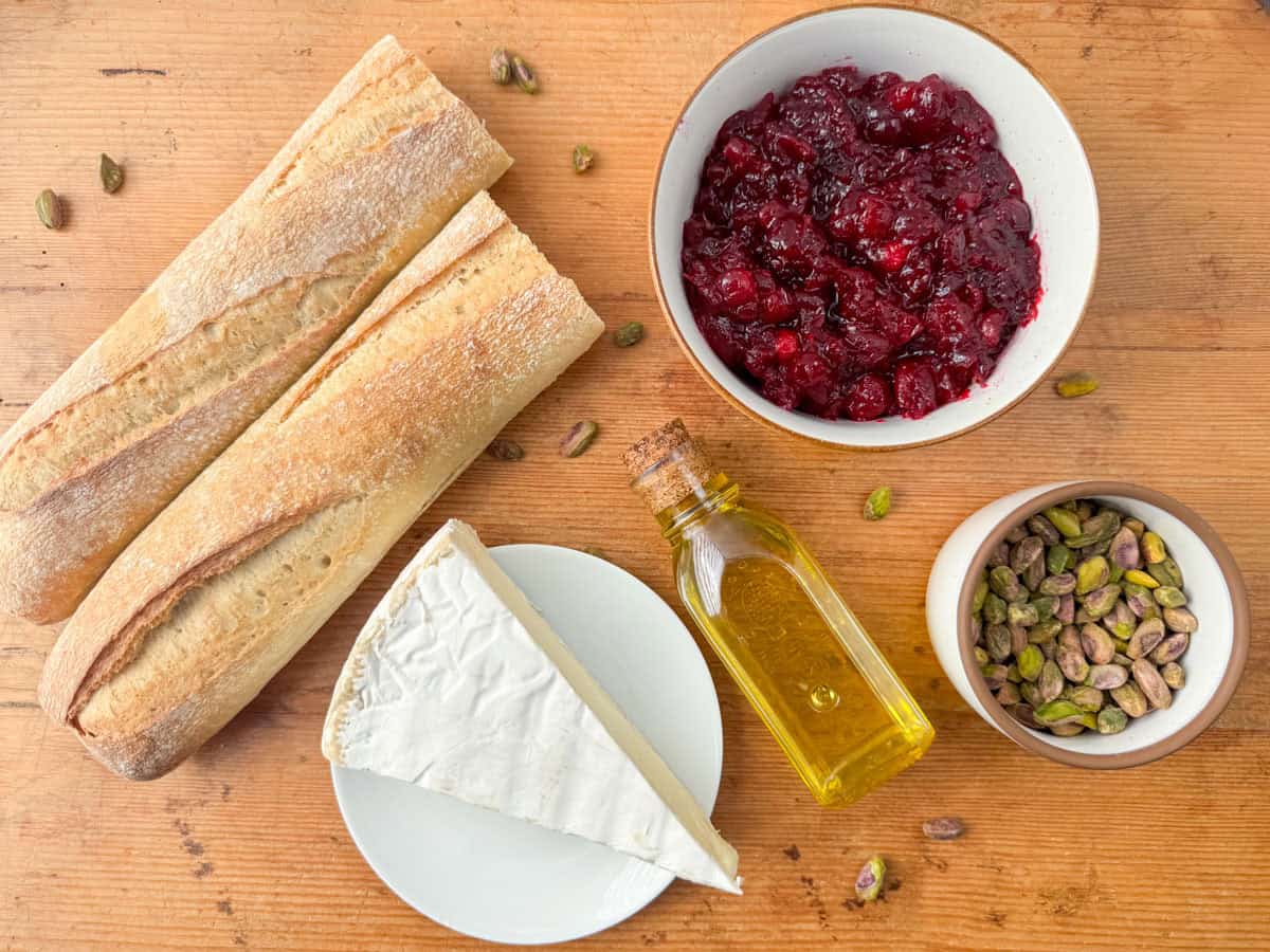 Ingredients needed to make cranberry brie crostini: baguette, brie, cranberry sauce and pistachios