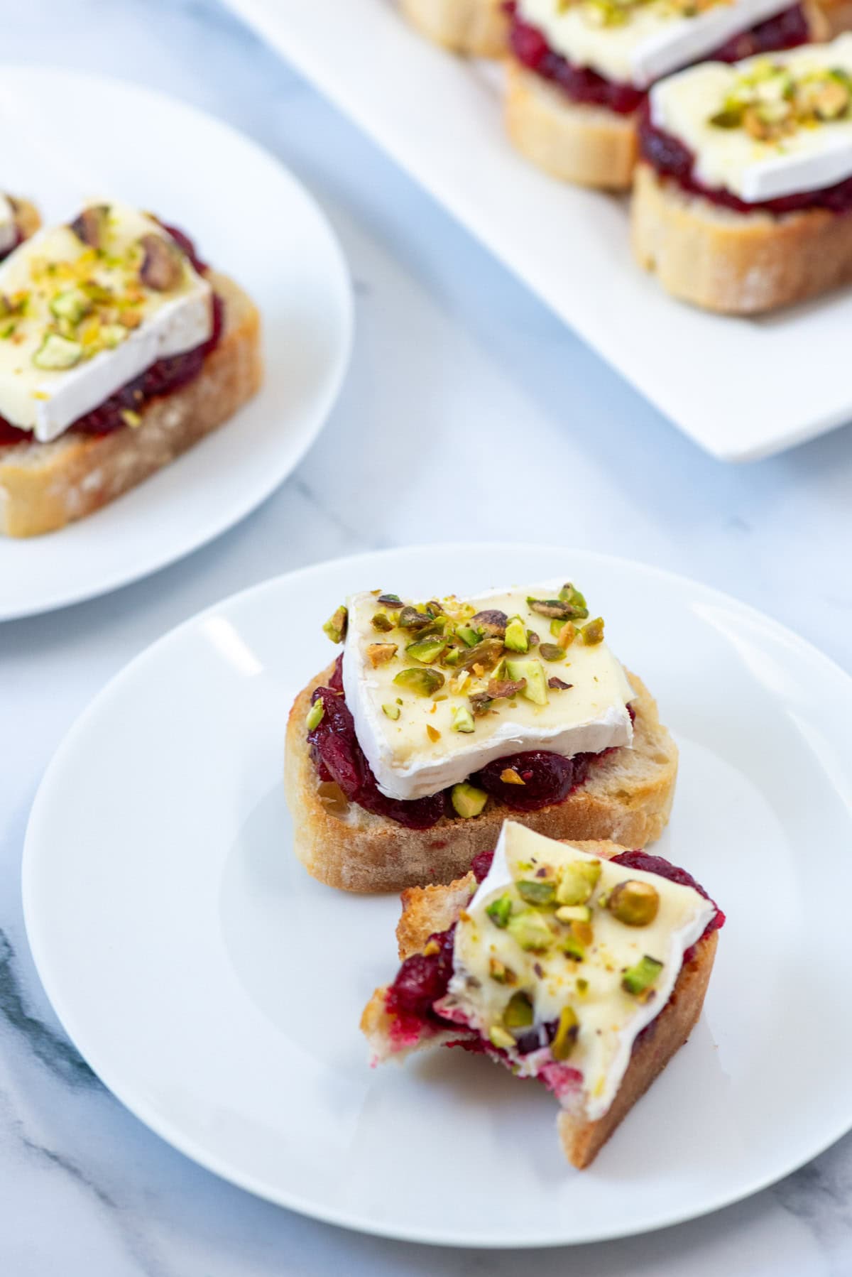 Cranberry brie crostini on a small plate in front of another small plate with cranberry brie crostini and a serving platter with cranberry brie crostini