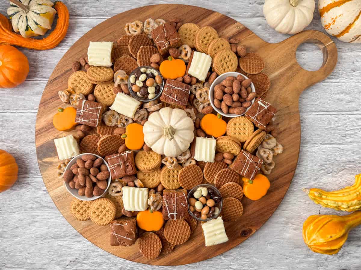Overhead view of finished fall dessert charcuterie board on a round, wooden board surrounded by small, mini pumpkins