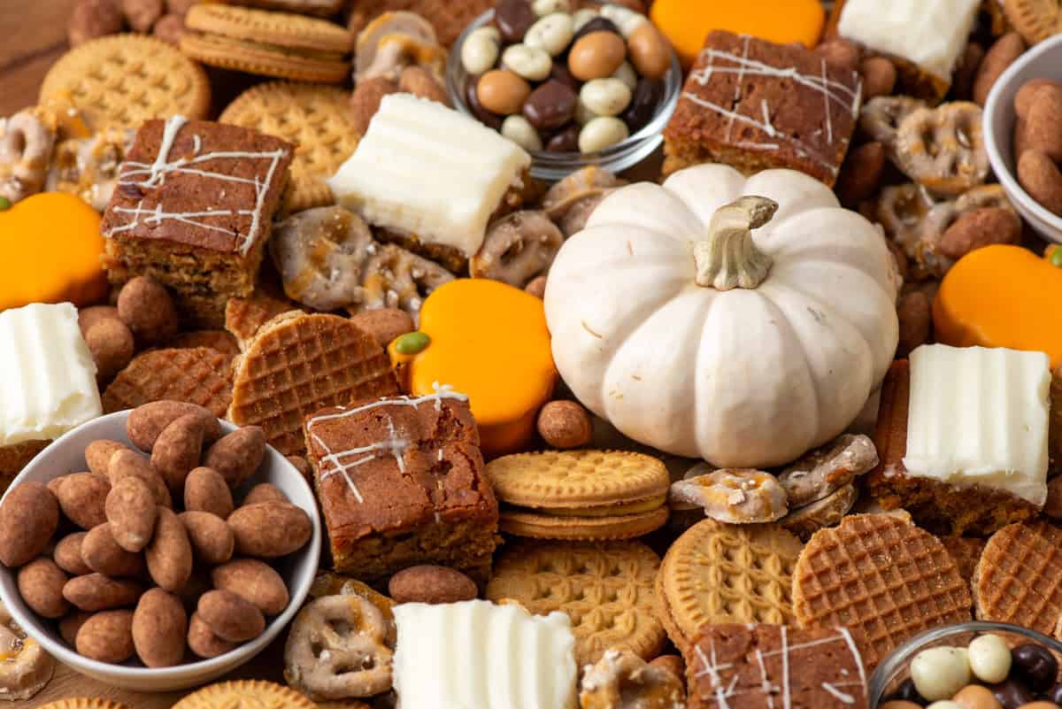 Overhead closeup view of a fall dessert charcuterie board made with mini pumpkin cakes, pumpkin brownies, pumpkin cookies, pumpkin covered pretzels, almonds and chocolate covered espresso beans