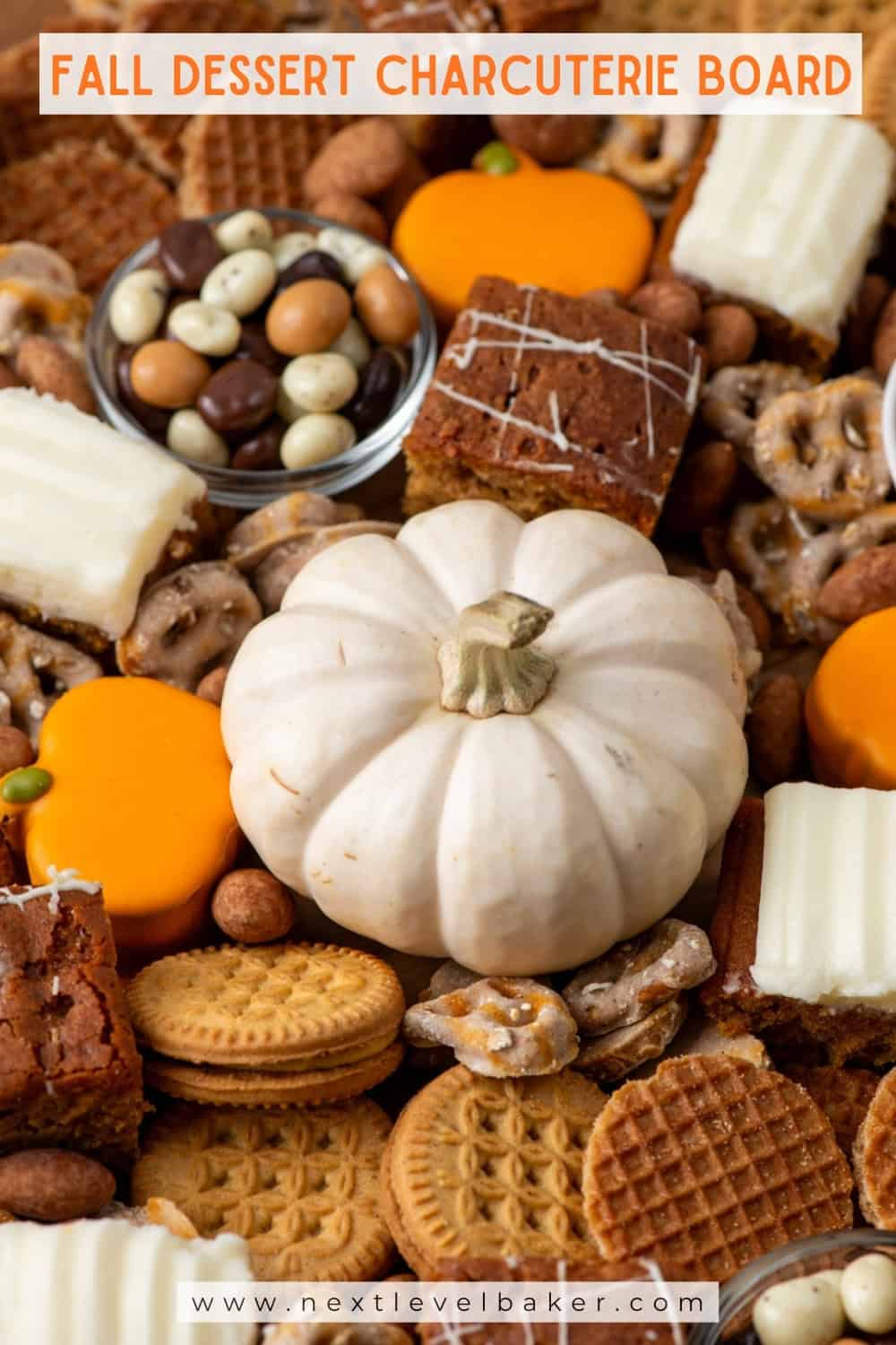 Overhead closeup view of a fall dessert charcuterie board made with mini pumpkin cakes, pumpkin brownies, pumpkin cookies, pumpkin covered pretzels, almonds and chocolate covered espresso beans with texts overlays saying Fall Dessert Charcuterie Board and www.nextlevelbaker.com